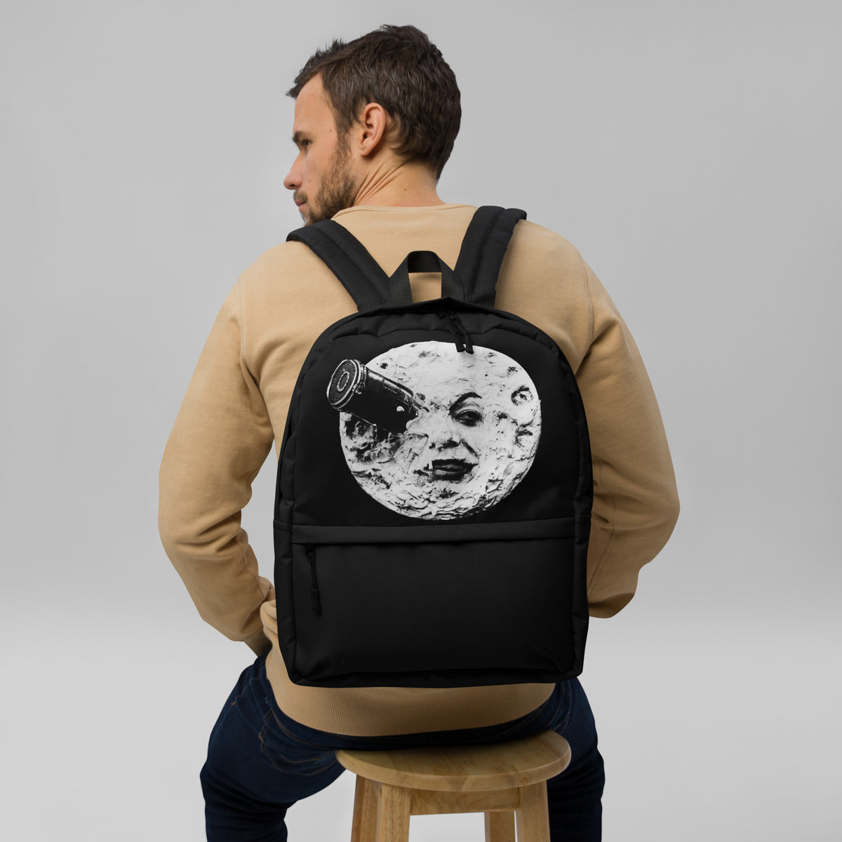 Black backpack with moon face graphic, worn from behind, top handle visible