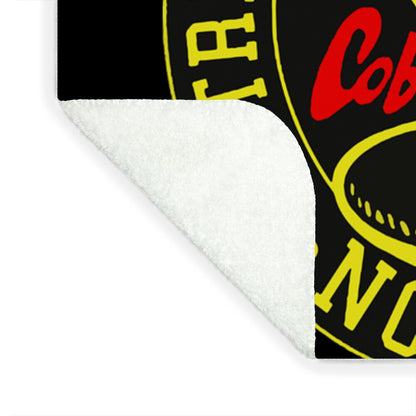 Corner of white plush blanket with part of a yellow circular emblem on black fabric