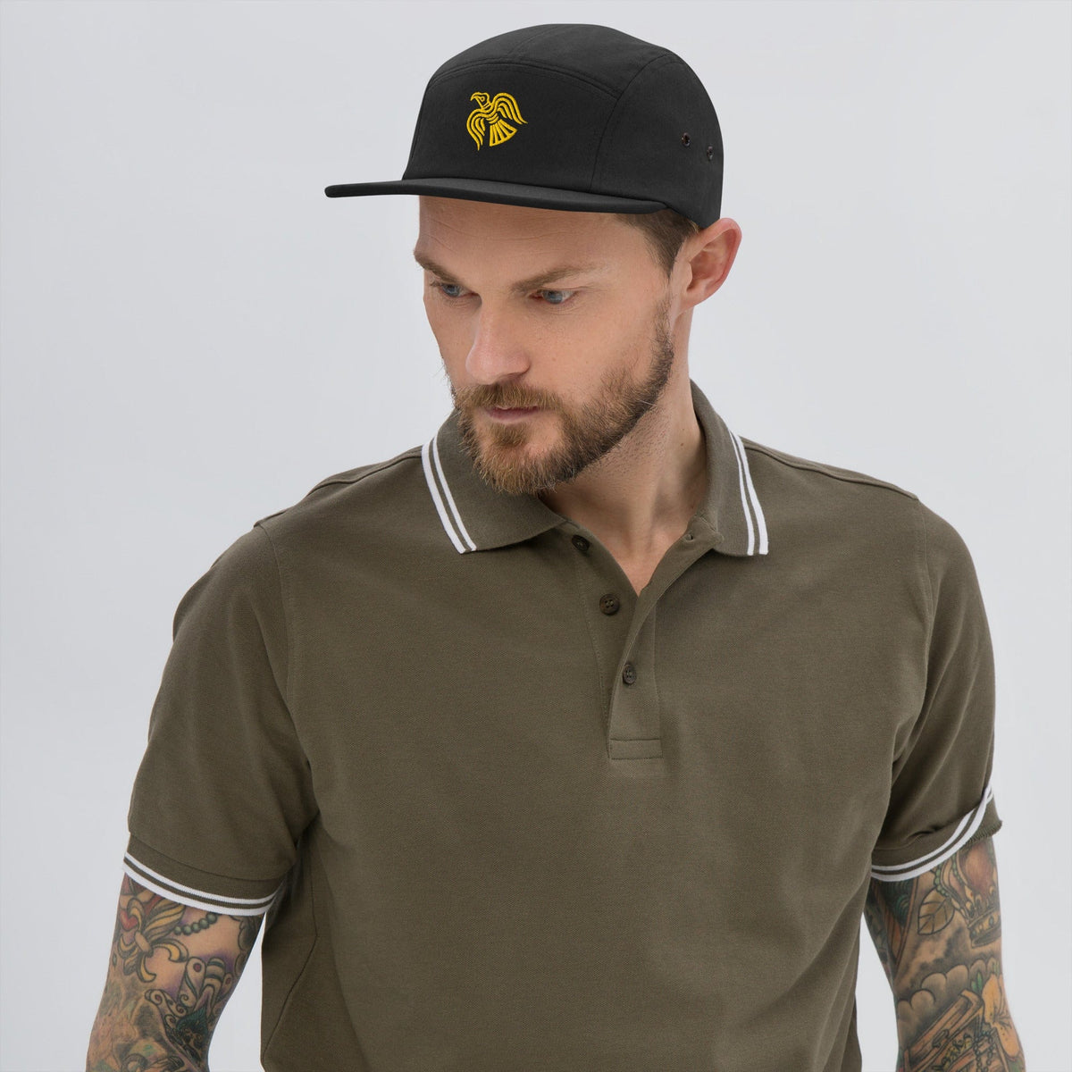 Black five-panel cap with embroidered yellow raven emblem worn by a man