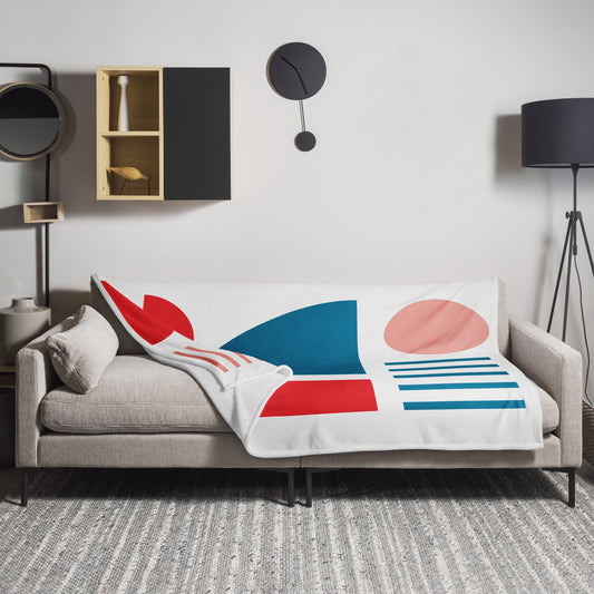 White throw blanket with red and teal geometric shapes and blue stripes, folded on sofa.
