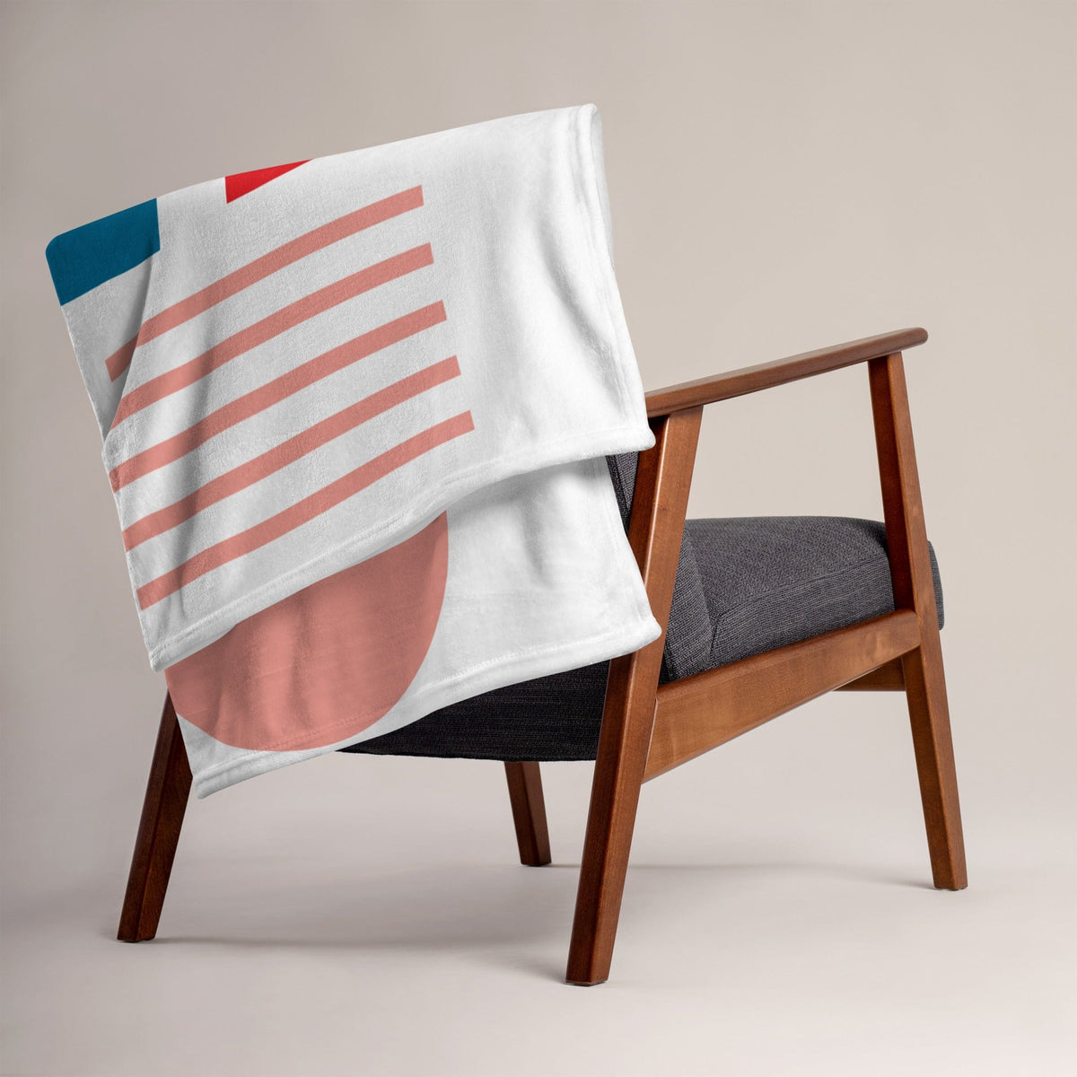 White throw blanket with coral-pink semicircle and teal striped band on wooden chair.