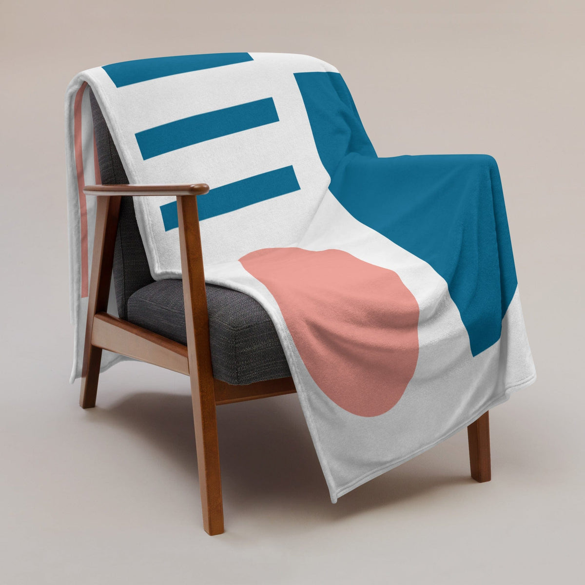 White throw blanket with bold teal blocks, blue lines, and pink curved shapes on chair.
