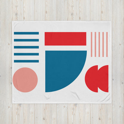 White throw blanket with large geometric shapes in blue, red, teal, and pink on display.