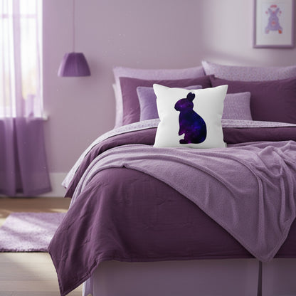 White throw pillow with dark purple galaxy rabbit graphic on front, on bed
