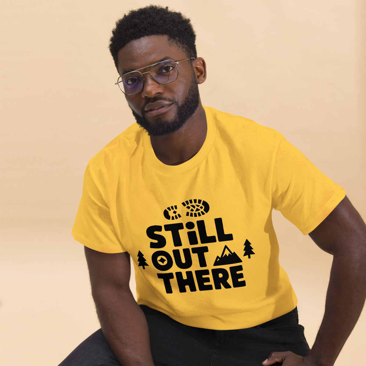 Yellow hiking T-shirt with black “Still Out There” logo graphic and paw-tree icon