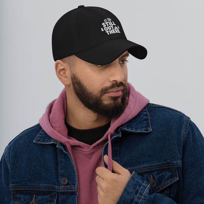 Black dad hat with embroidered “STILL OUT THERE” logo on front and curved brim.