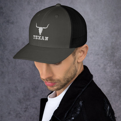 Olive/dark gray trucker hat with white bull head and “TEXAN” lettering on the front.