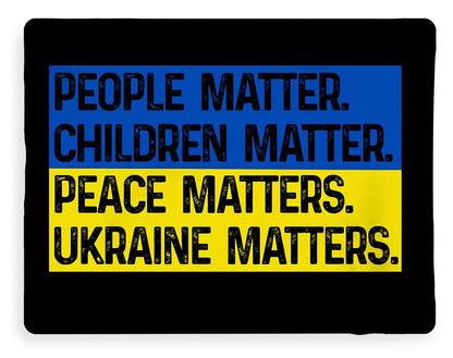 Black blanket with blue and yellow slogan print: CHILDREN MATTER, PEACE MATTERS