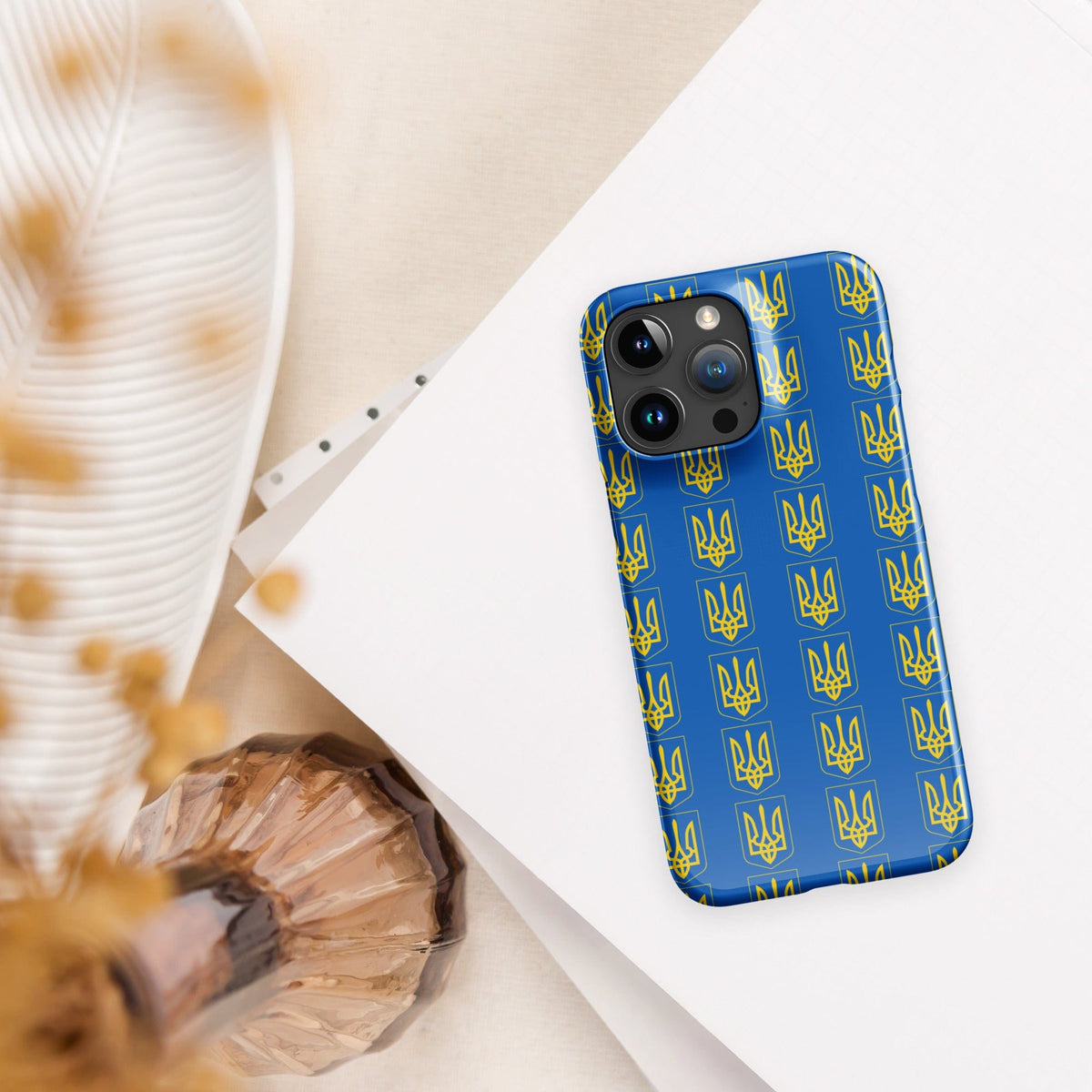 iPhone phone case with blue Tryzub trident pattern, tilted on white paper