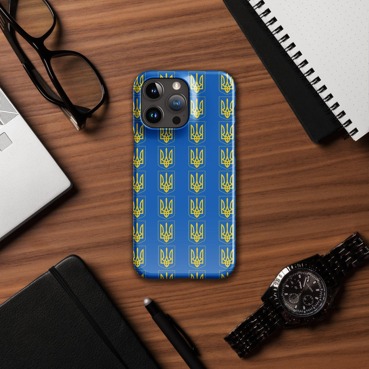 iPhone phone case with blue Tryzub trident pattern, flat lay with accessories