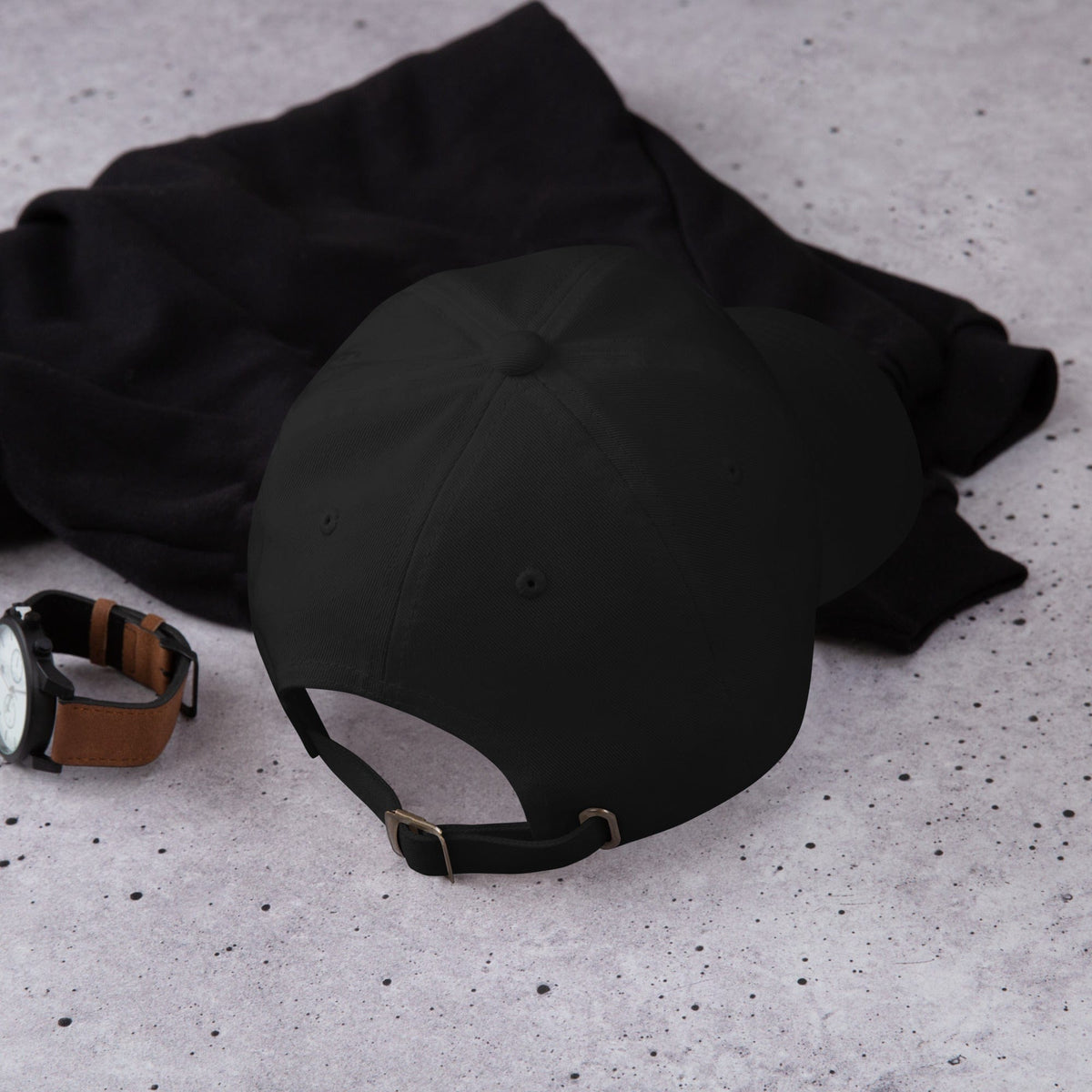 Black embroidered cap with strap visible, lying on black fabric