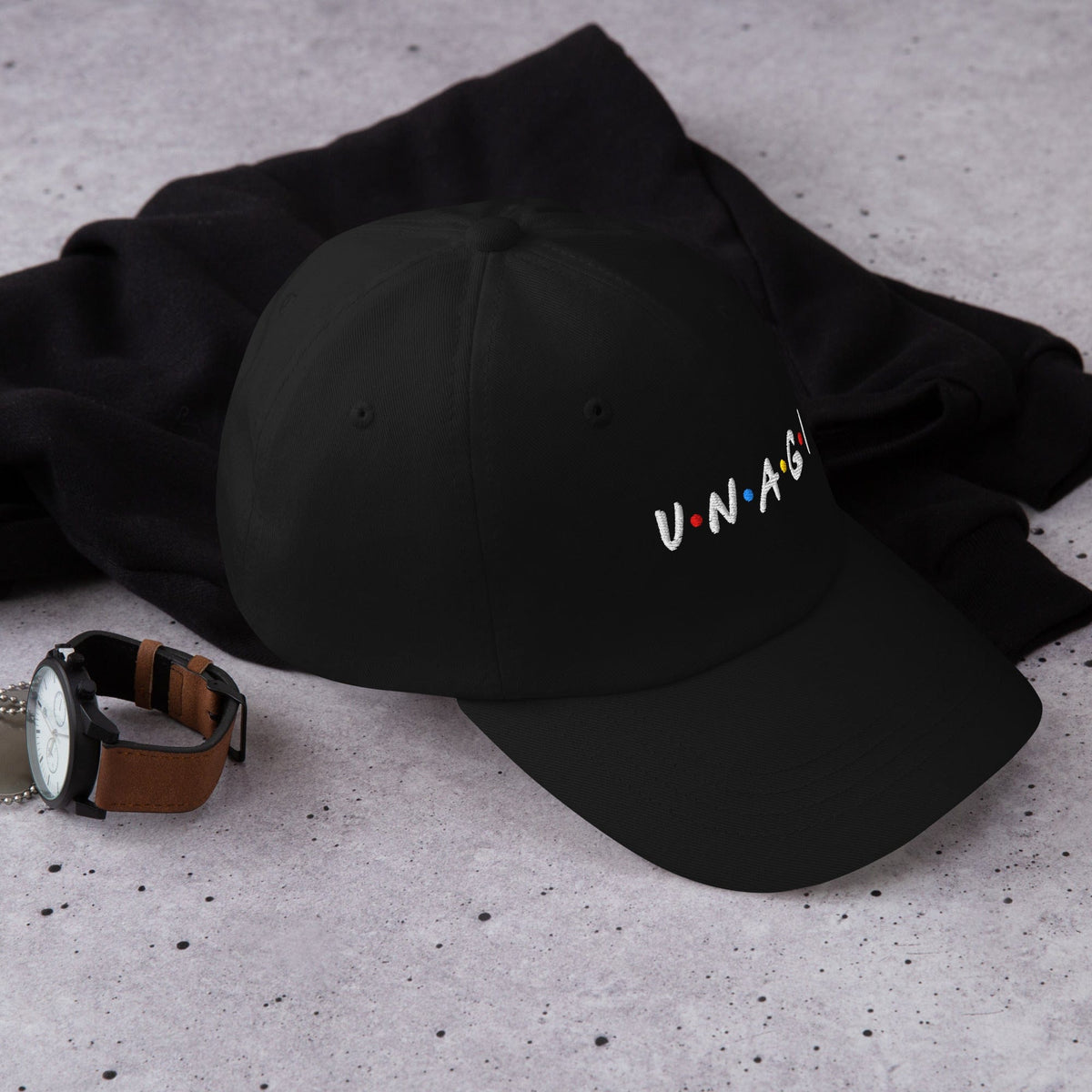 Black embroidered cap with V.N.A.G.I logo on front, lying on black fabric