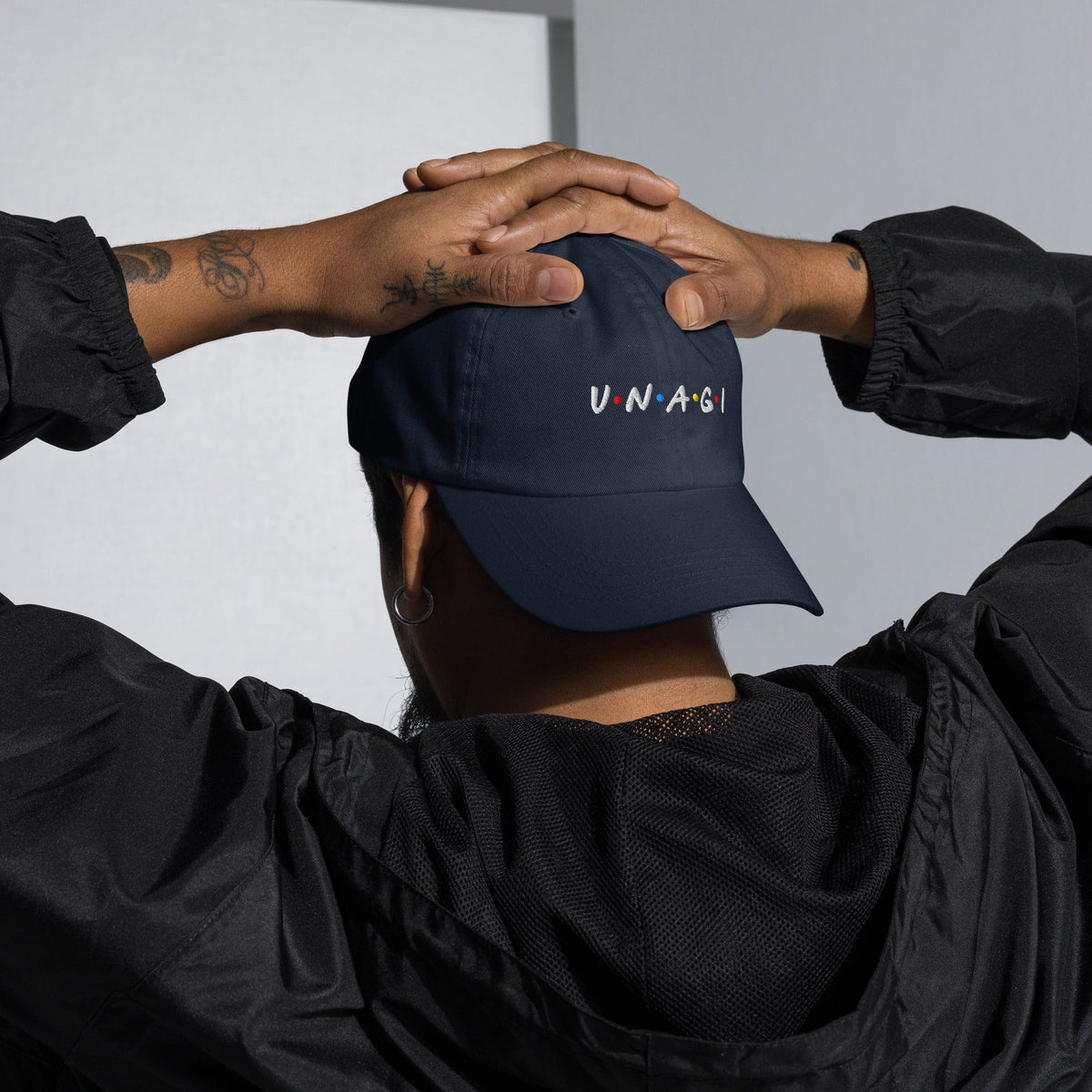 Navy embroidered cap with V.N.A.G.I logo on front, held in hands by wearer