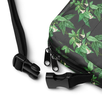 Utility crossbody bag detail: green leaf floral fabric, black strap and zipper pull